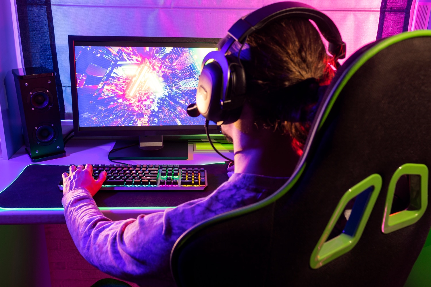 A gamer wearing a headset plays at a colorful setup, focused on a vibrant action-packed video game