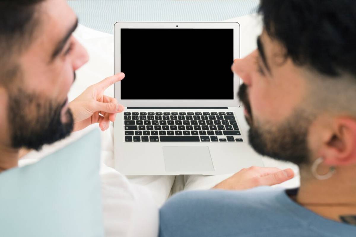 Two men looking at a laptop with a blank screen, discussing something intently.