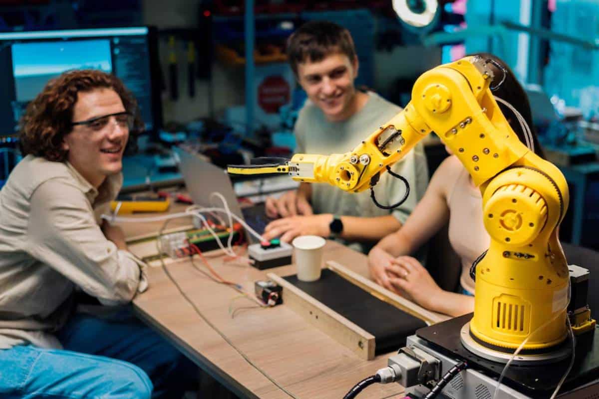 Two young engineers programming a robotic arm in a technology lab filled with electronic equipment.