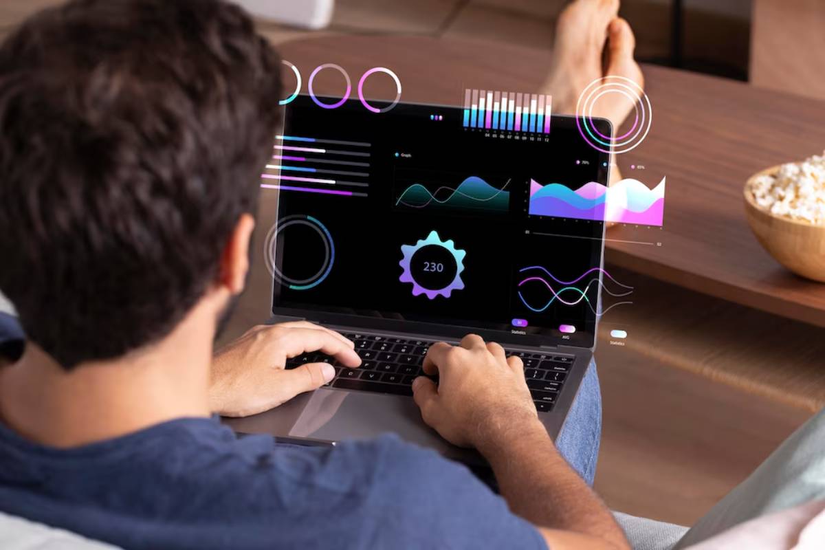 A man sits on a couch, using a laptop displaying colorful data visualizations