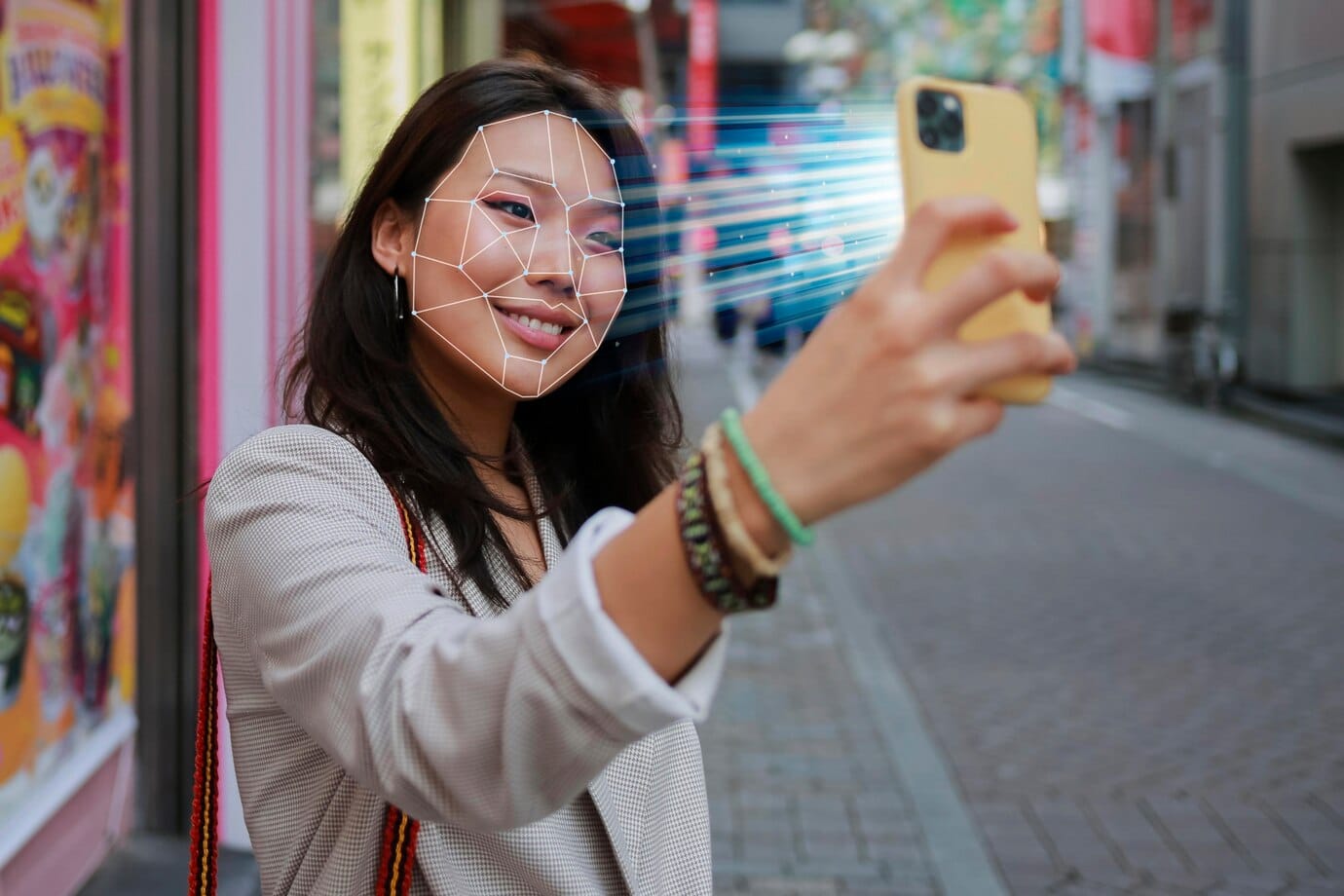 Young woman uses facial recognition on her phone in a colorful urban area.